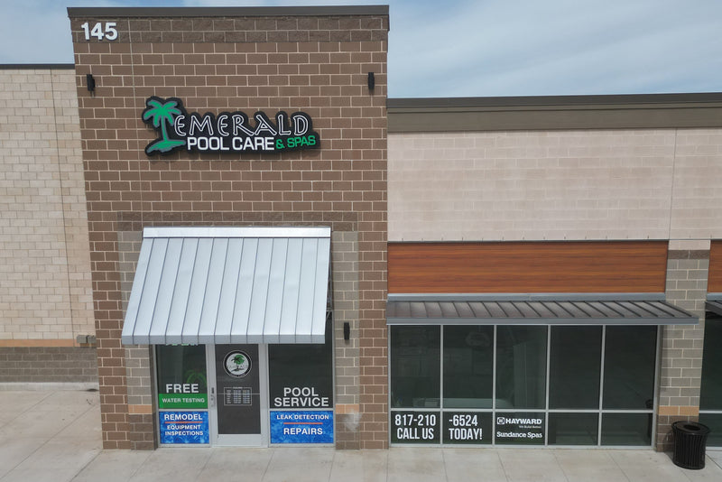Front exterior of Emerald Pool Care & Spas at 149 E Bonds Ranch Rd, showing a brick facade, storefront awnings, large glass windows, and a paved sidewalk under a blue sky.